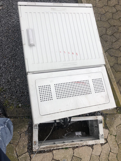 Outdoor-Verteilerkasten mit Markierung "Kabel Deutschland". Kasten auf dem Boden liegend, Sockel in der Erde, Kabel freiliegend.