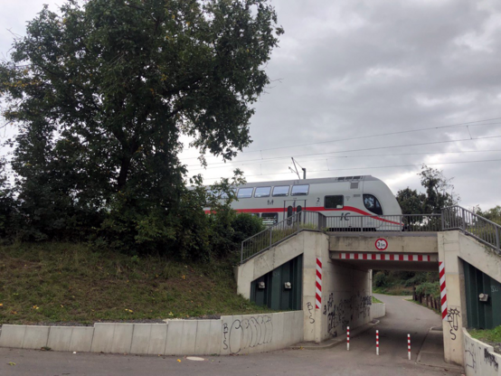 Weiß lackierter IC mit rotem Streifen auf Bahndamm/schmaler Bahnbrücke über einen Feldweg. 