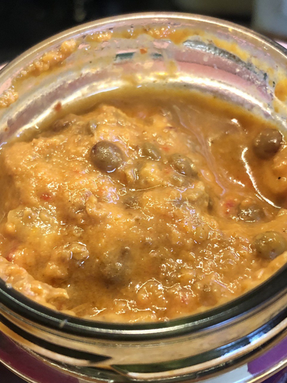 Blick ins Glas. Hell-Orange, eher flüssige Pampe mit kleinen, roten Flecken (Tomate) und braunen Kügelchen (Linsen). Etwas klare Flüssigkeit in Senken.