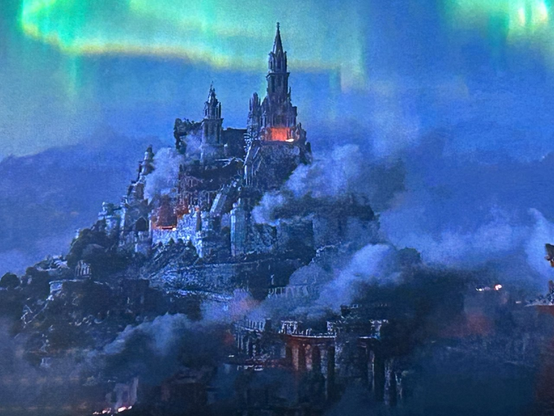 Berg mit Schloss bei Dunkelheit. Gebäude und Umgebung stark beschädigt und teilweise brennend. Polarlichter über der Szene.