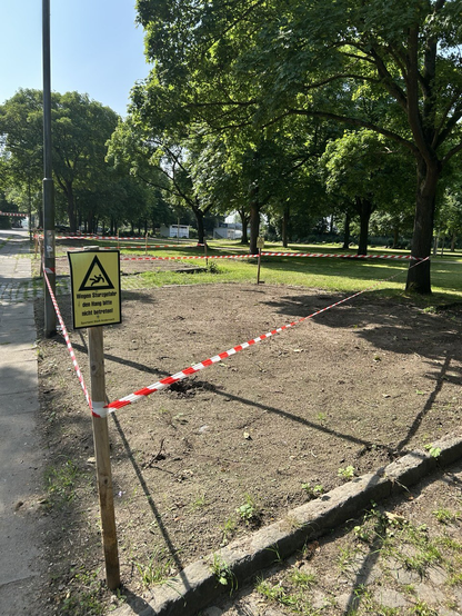Blumenbeet neben Gehweg, mit Flatterband abgesperrt. "Wegen Sturzgefahr den Hang bitte nicht betreten!". Es gibt keinen Hang.