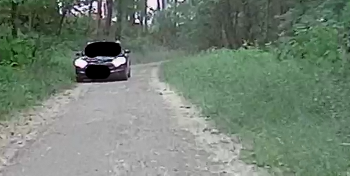 Unbefestigter Waldweg mit ~2-3m Breite. Ein schwarzer Skoda PKW kommt entgegen. Er fährt bereits im Grün nebenan um Platz zum passieren zu schaffen.