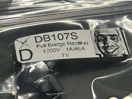 Kleines, rechteckiges Label im Querformat auf einer Tüte mit Bauteilen

Links: Monochrom gedithertes Bitbastelei-Logo mit großem D darunter
Mitte: DB107S (größer geschrieben) Full Bridge Rectifier · 1000V · 1A/45A · 1V
Rechts Monochrom gedithertes Foto eines breit grinsenden Mehdi (ElectroBOOM) 