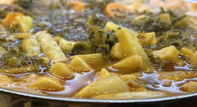 Nahaufnahme eines Kochtopfes. Flüssigkeit im inneren geht bis Zum Rand. Dinnen sind Rübenstifte, Grünkohl und Möhrenscheiben erkennbar.