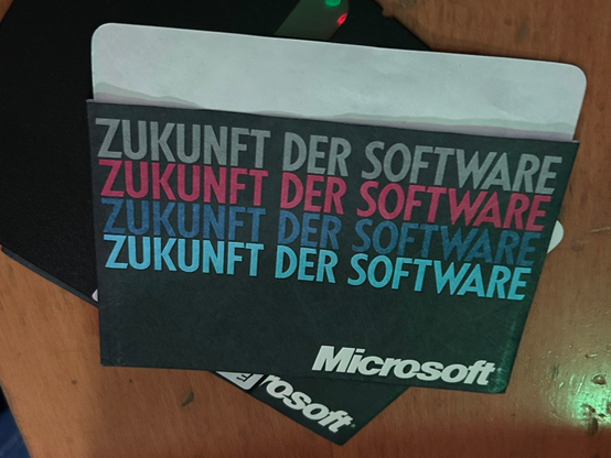 Hülle einer 5¼" Floppy in dunklem Grau
Text groß in Hellgrau, schwachem Rot, dunklem Blau und Cyan untereinander je "ZUKUNFT DER SOFTWARE"

Unten Rechts das Microsoft-Logo, welches 1987-2012 genutzt wurde