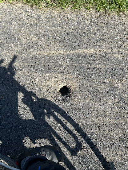 Unbefestigter Feldweg. In der Mitte ~10cmØ Loch, Tiefe nicht erkennbar. Schatten eines Rades daneben.